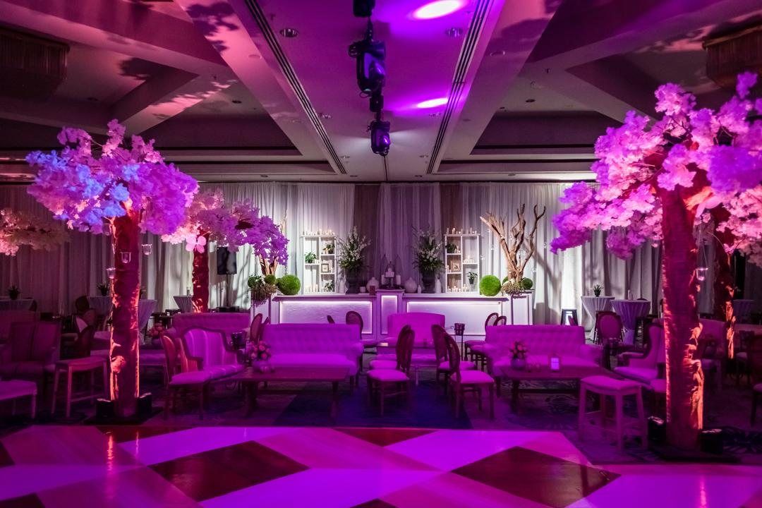 Ballroom in pink light with blossom trees, white lounges and a checkered dance floor