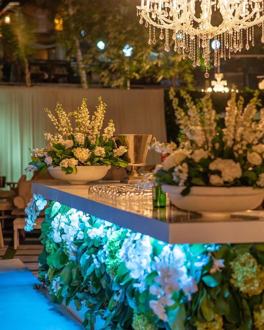 Bar wrapped in white orchids and hydrangeas, lit from within, beneath a crystal chandelier