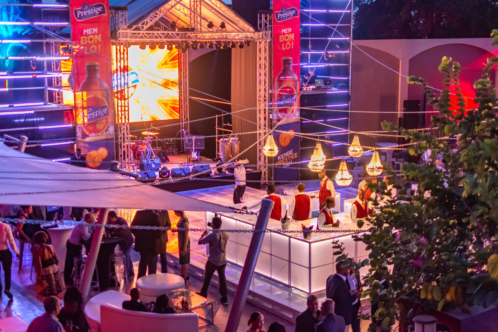 Open-air corporate launch at dusk with stage, bar and chandeliers