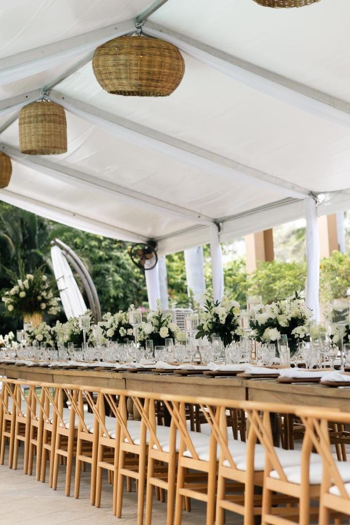 Long table under a white tent with rattan pendants and white florals